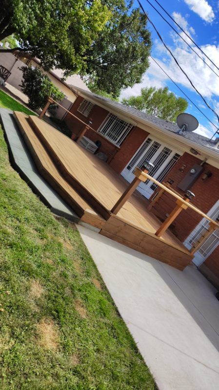 Wooden deck with steps leading to a red-brick house, a wooden handrail, and green grass.