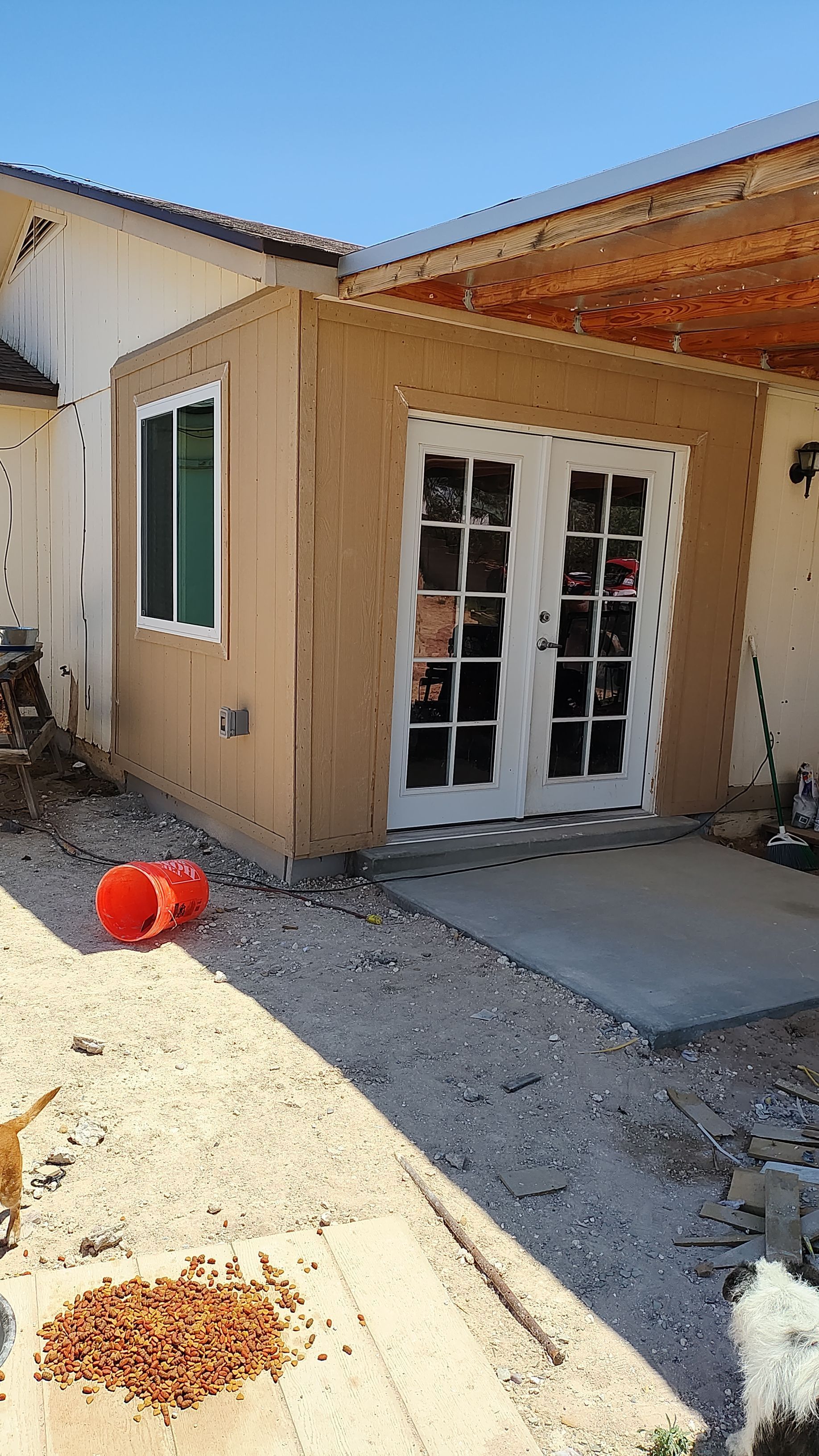 New outdoor structure with stucco walls and white French doors, next to a house.