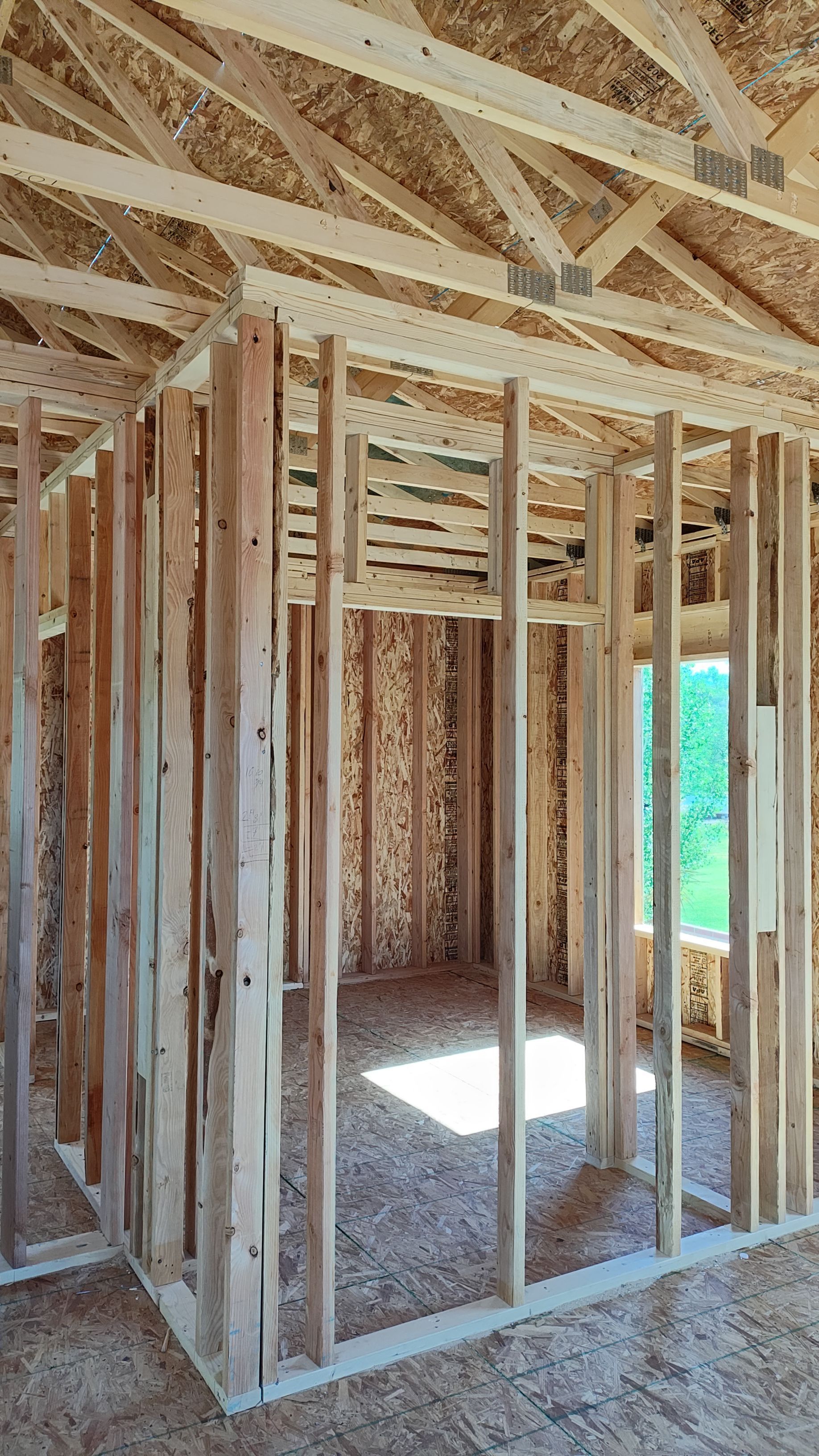 Interior wood framing of a room under construction; studs, joists, and window opening.