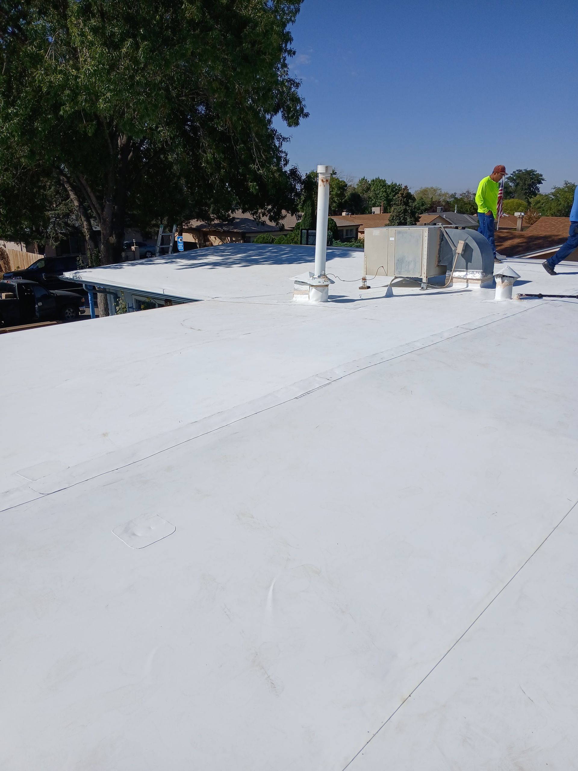 White commercial roof with HVAC units and a worker in the background.