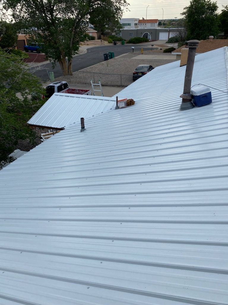 White corrugated metal roof with chimneys, looking over a residential neighborhood.