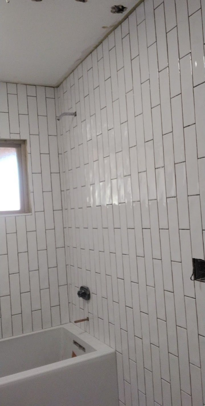 White tiled bathroom with a tub, window, and shower fixtures.