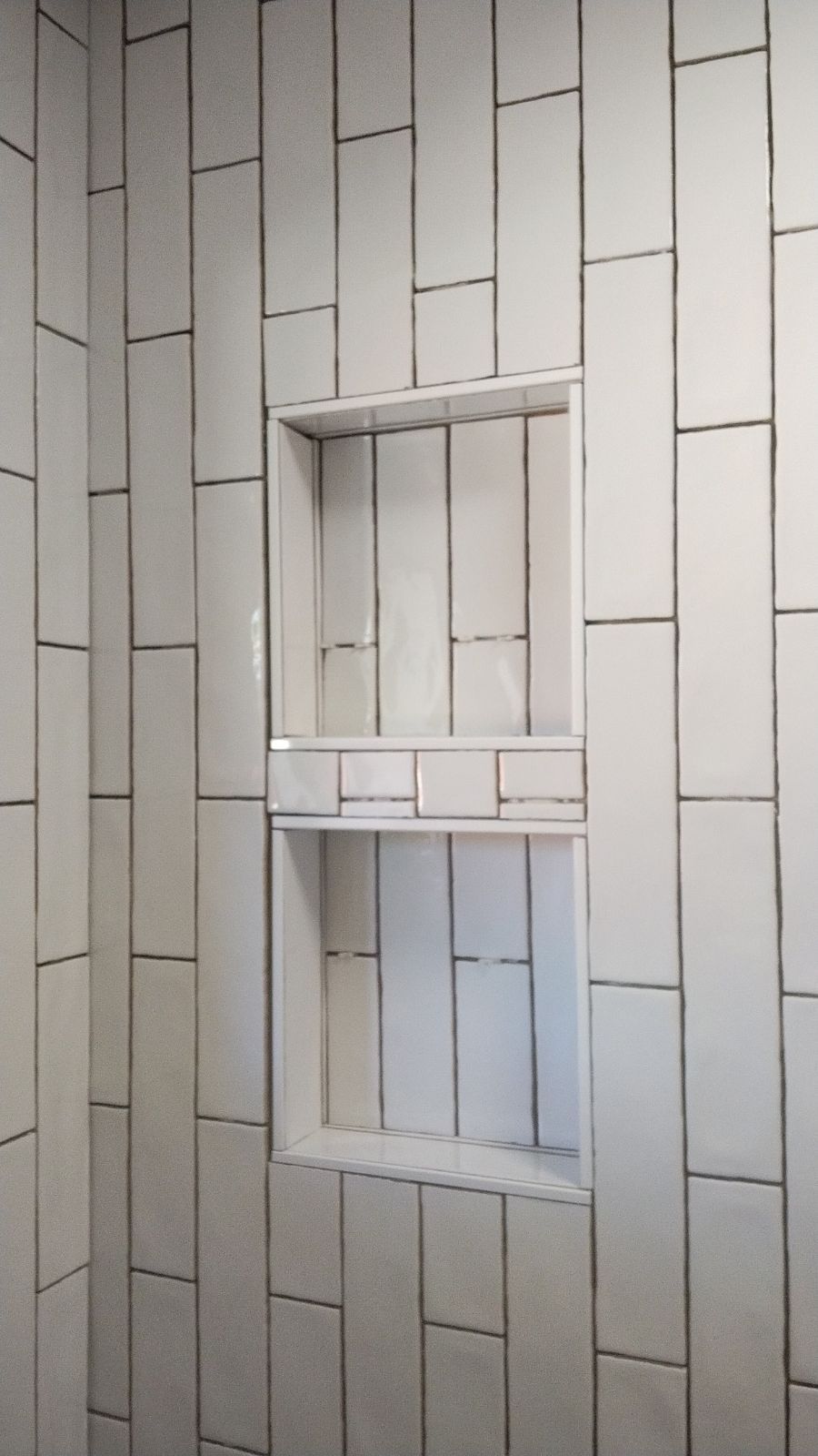 White tiled shower wall with built-in shelf.