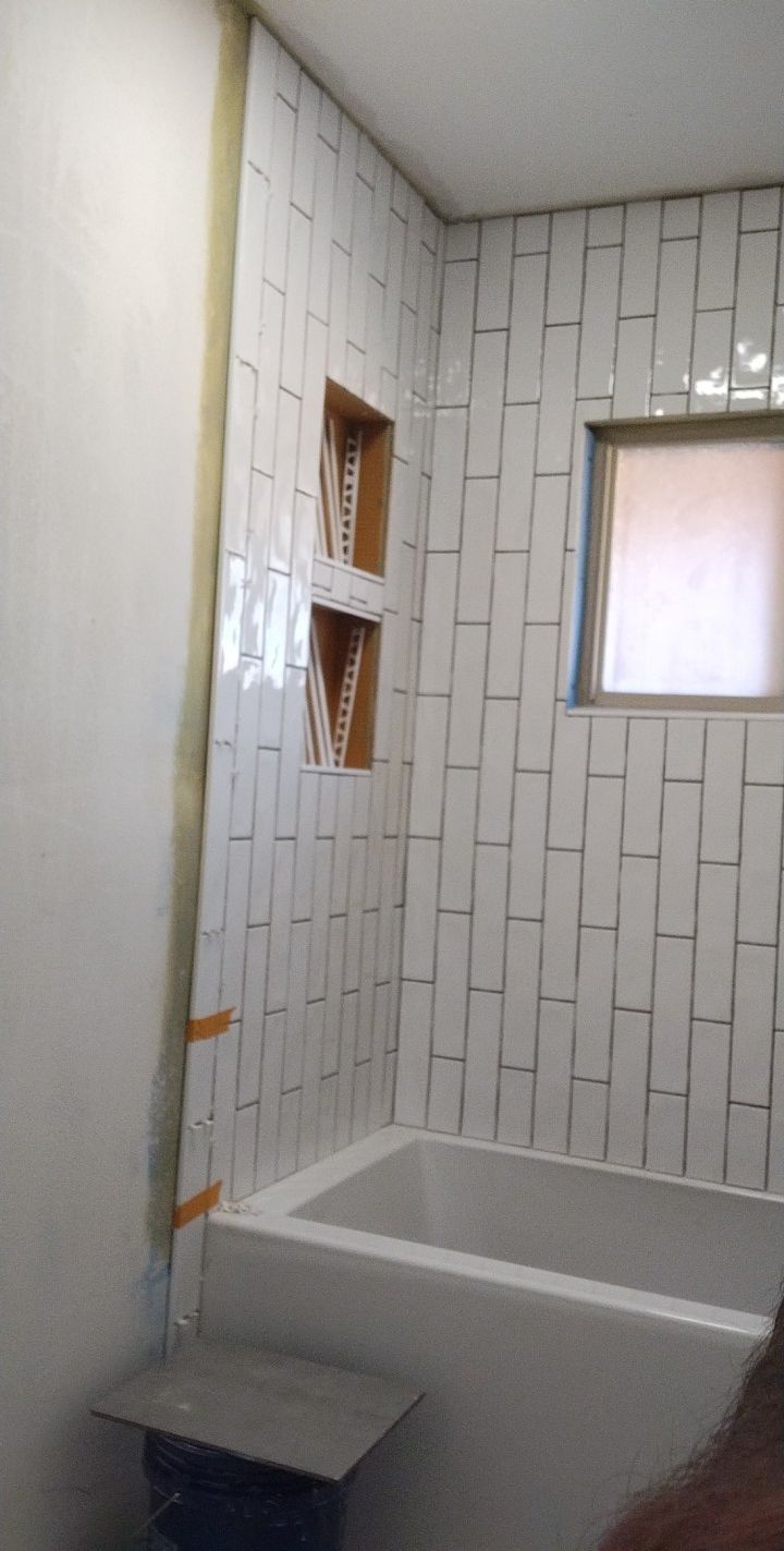 Bathroom with white subway tile walls, a recessed shelf, and a bathtub.