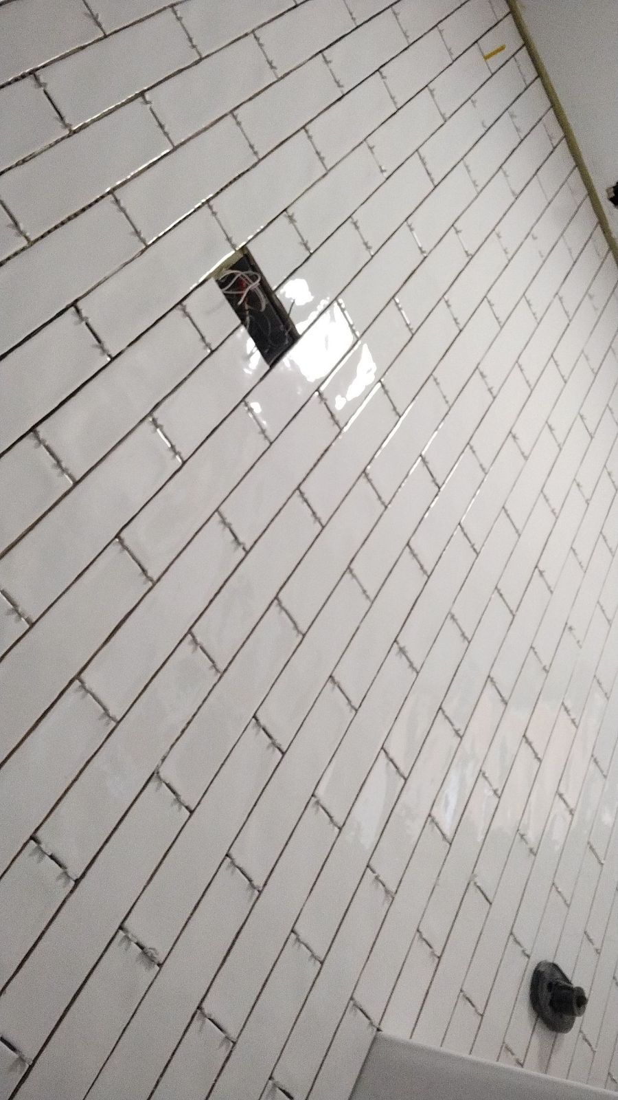 White subway tile bathroom wall with a rectangular opening and dark grout.