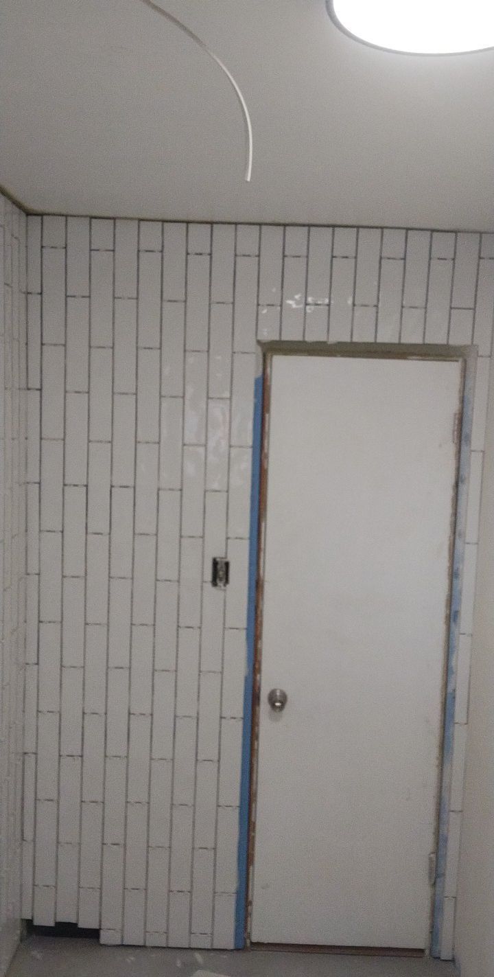 White rectangular tiles on a wall with a white door and light fixture.