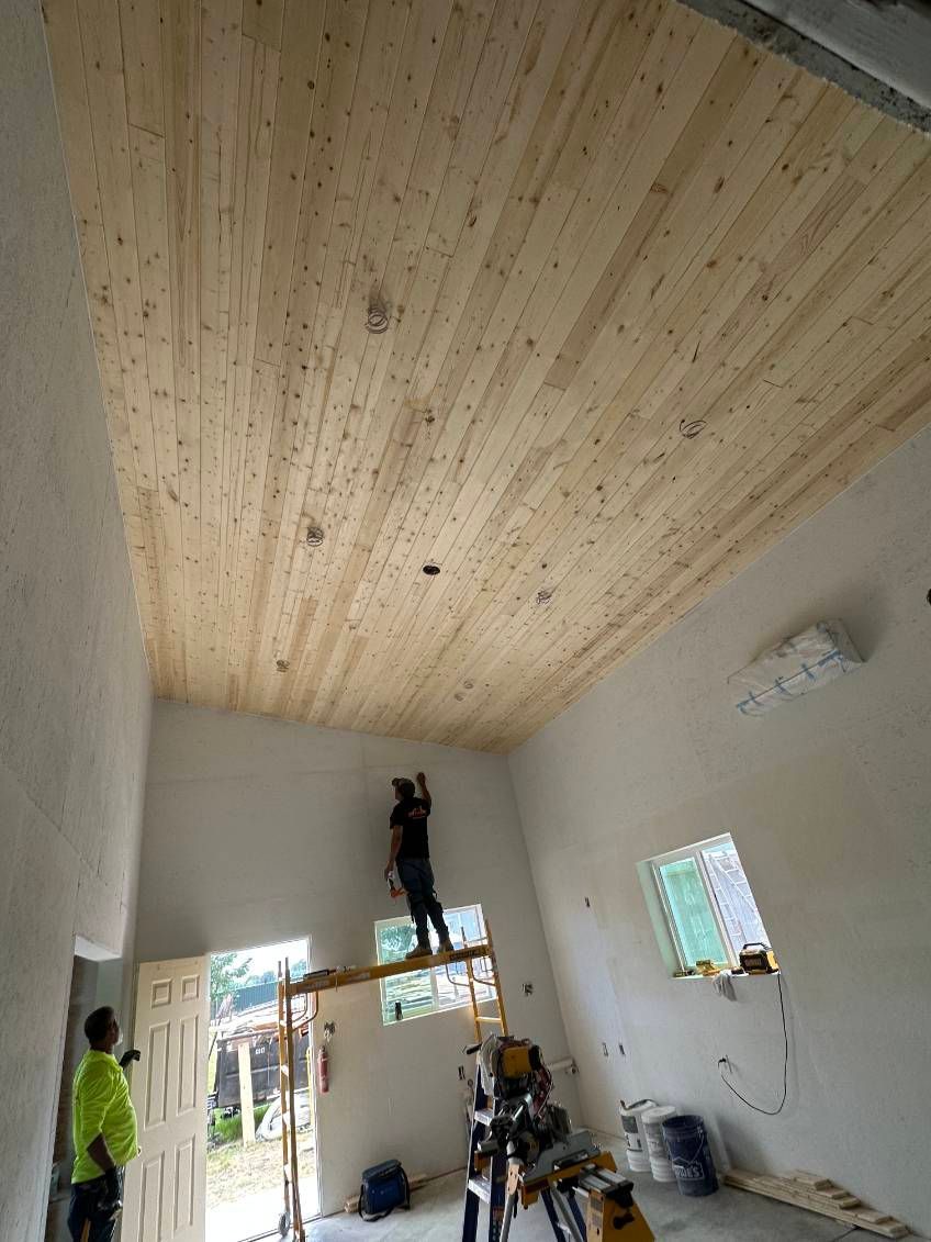 Workers installing a wooden plank ceiling in a room with white walls and a doorway.