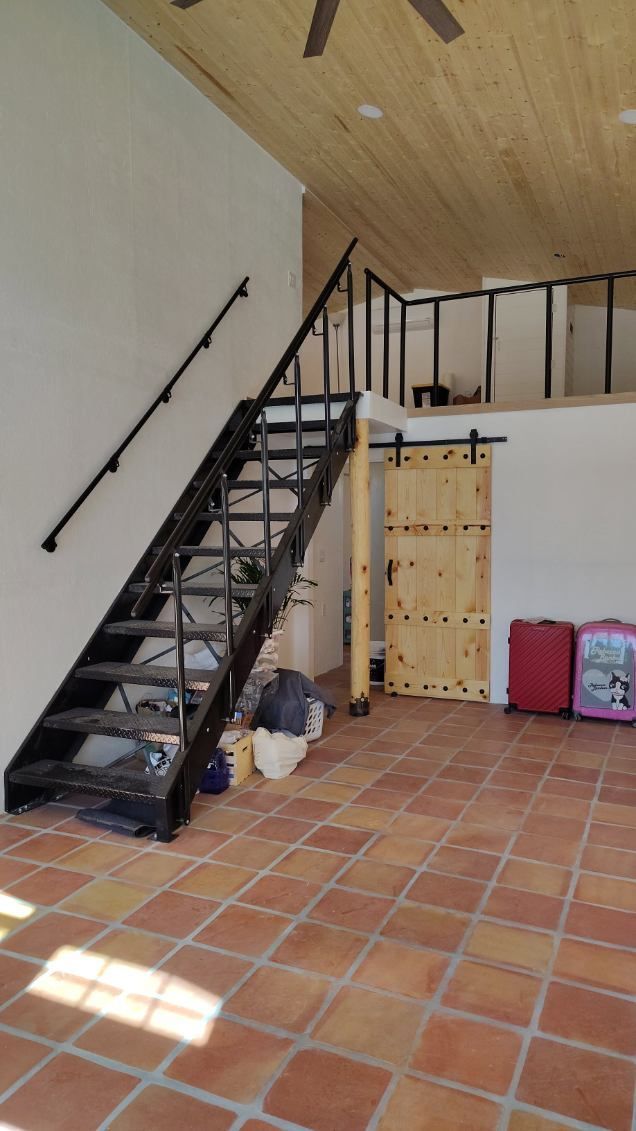 Interior with stairs leading to a loft. Black metal railing, terra cotta floor, wooden door.