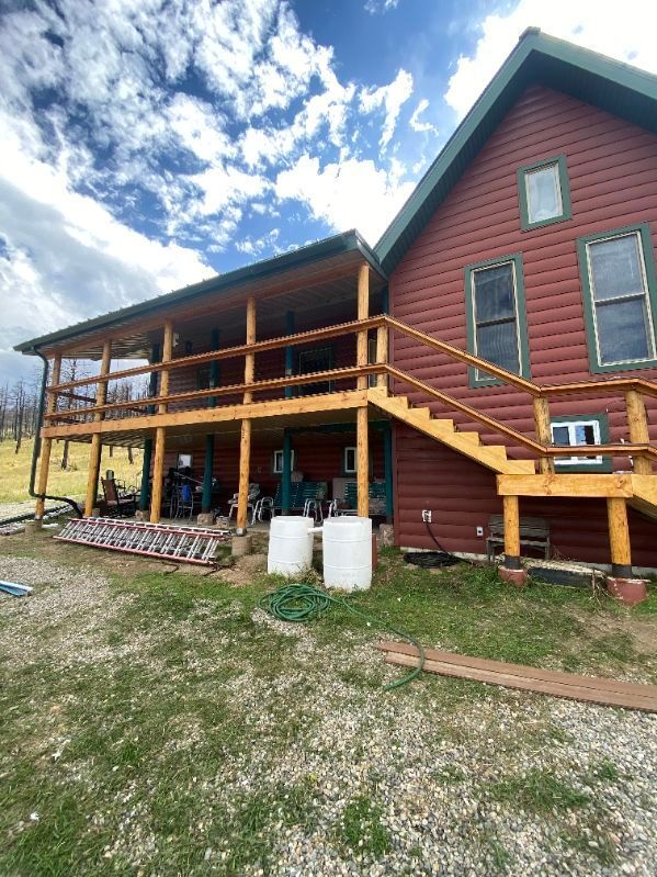 Red log cabin with wooden deck and stairs, two white barrels sit below.