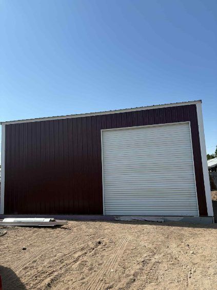 Brown and white metal building with a garage door against a clear blue sky.
