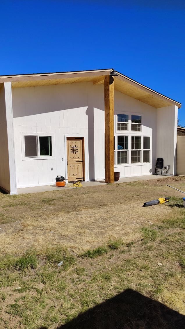 White stucco building with wooden door, windows, and large, brown support beam.