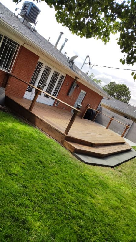Wooden deck with stairs in backyard, red brick house, green grass.