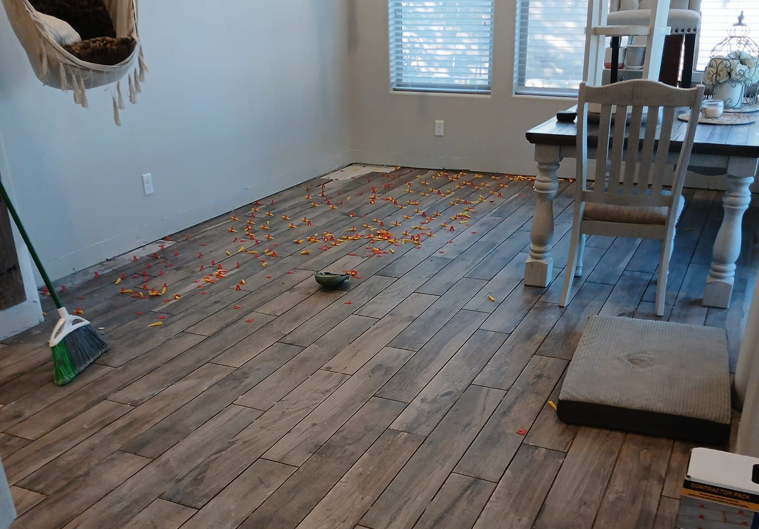 Wooden floor covered in scattered candy, broom nearby. Dining table and chairs in the background.