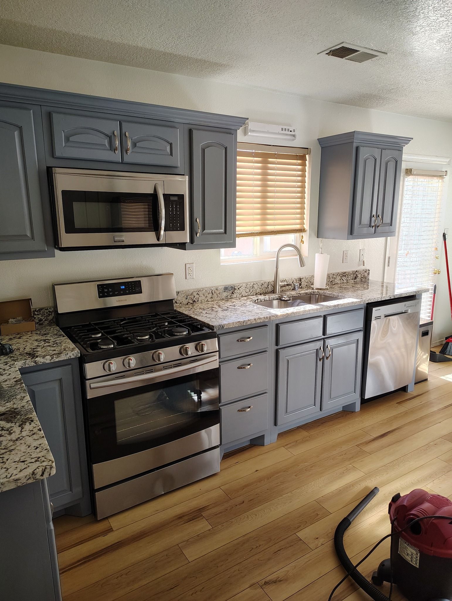 Blue-gray kitchen cabinets with stainless steel appliances and light wooden floors.