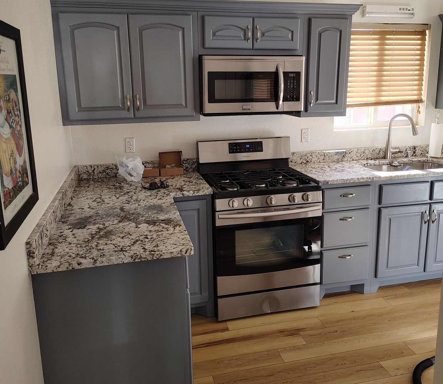 Kitchen with gray cabinets, stainless steel appliances, granite countertops, and wood floors.