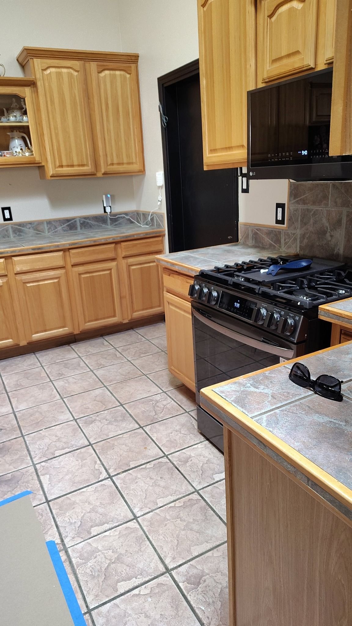 Kitchen with light wood cabinets, tile floor, black stovetop, and gray countertops.