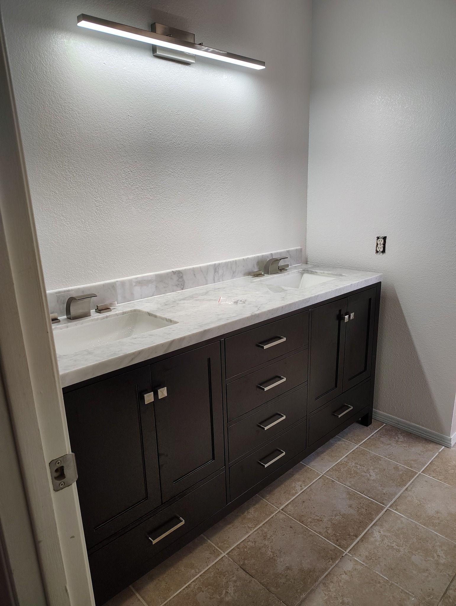 Dark bathroom vanity with a white countertop, sinks, and a light fixture above.