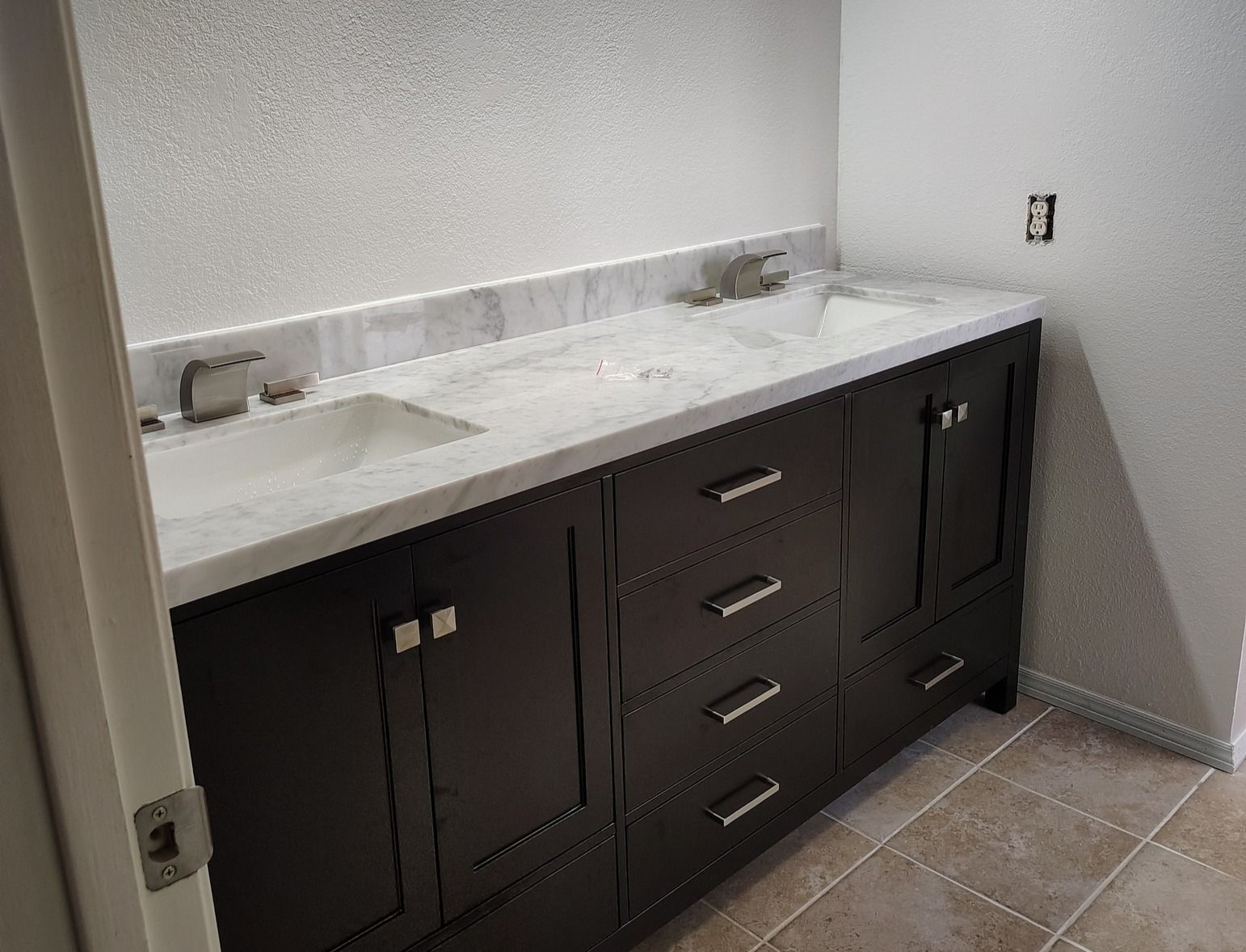 Dark bathroom vanity with a white countertop, sinks, and a light fixture above.