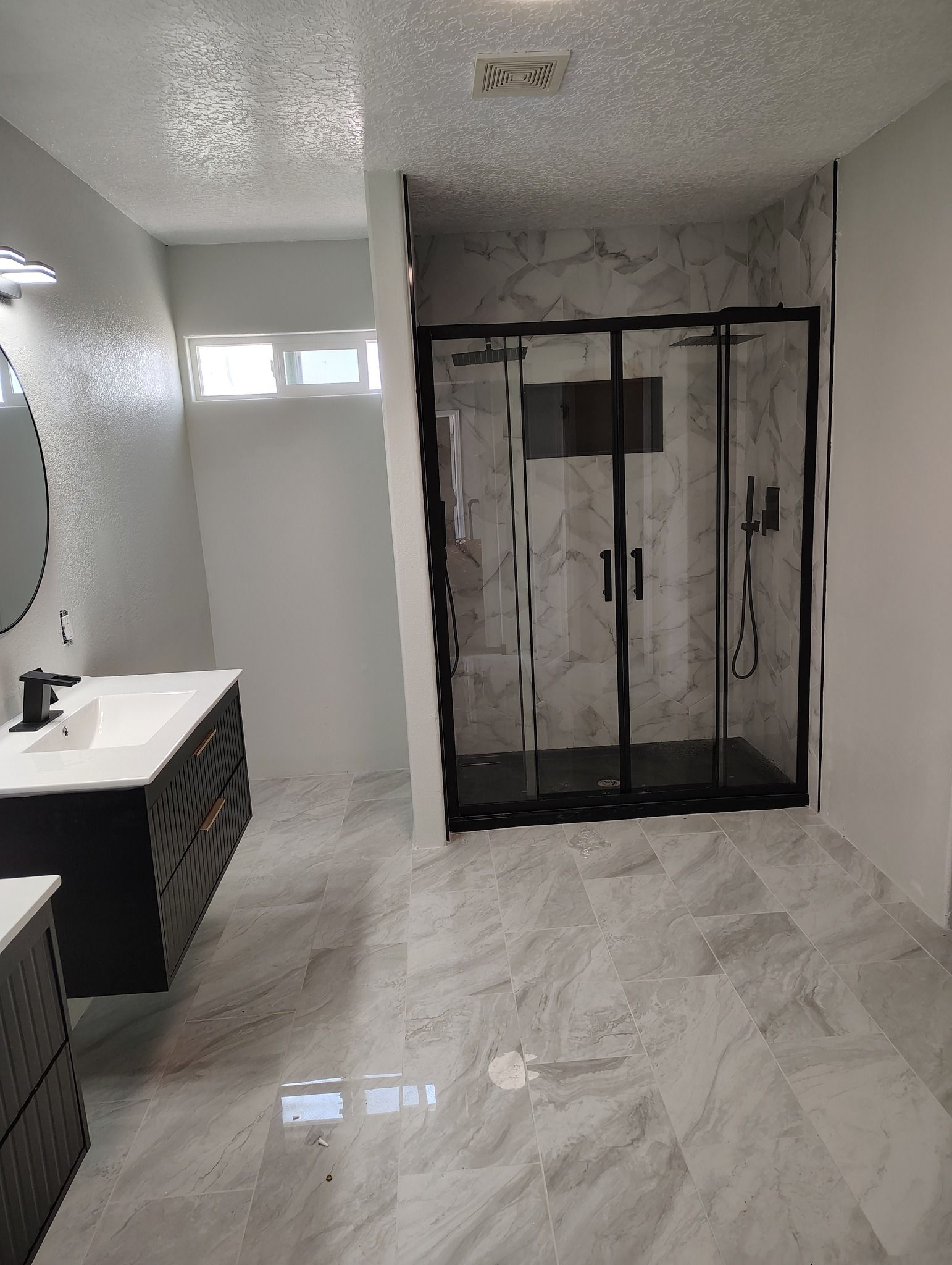 Modern bathroom with gray marble tile, black-framed shower, and dark vanity.