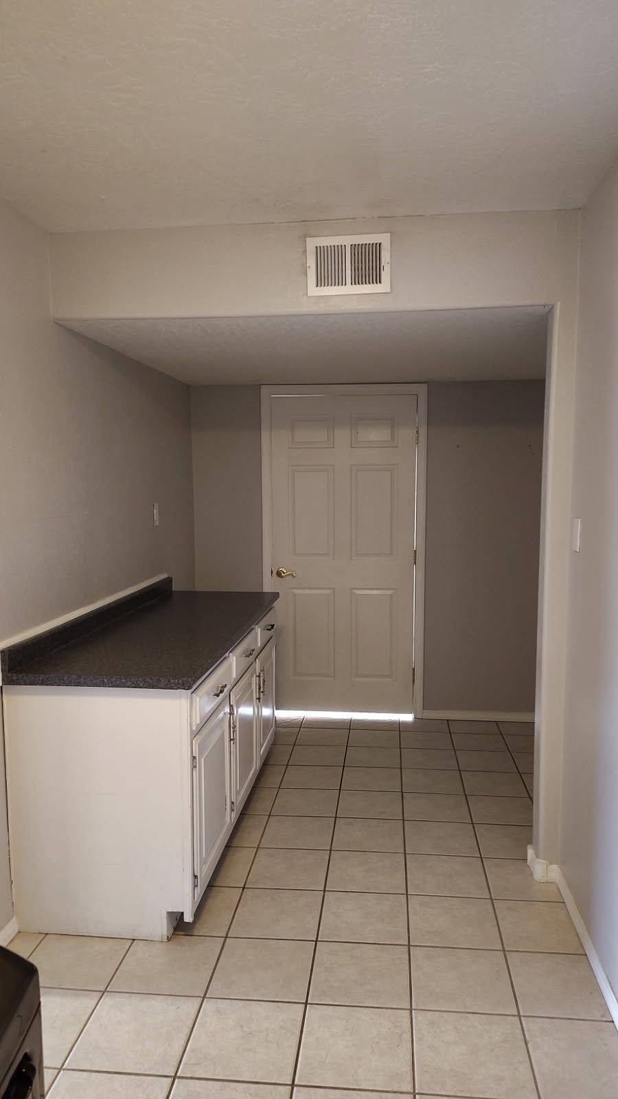 Kitchen with white cabinets, dark countertop, and door. Gray walls and tile floor.