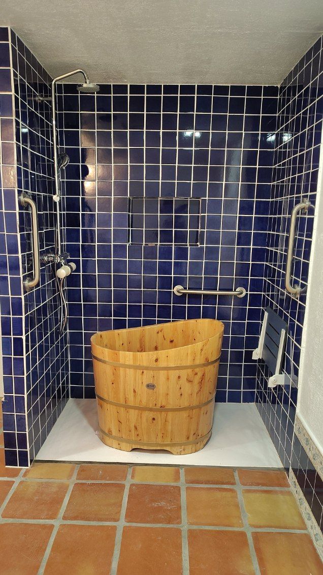 Wooden soaking tub in a tiled shower stall with grab bars.