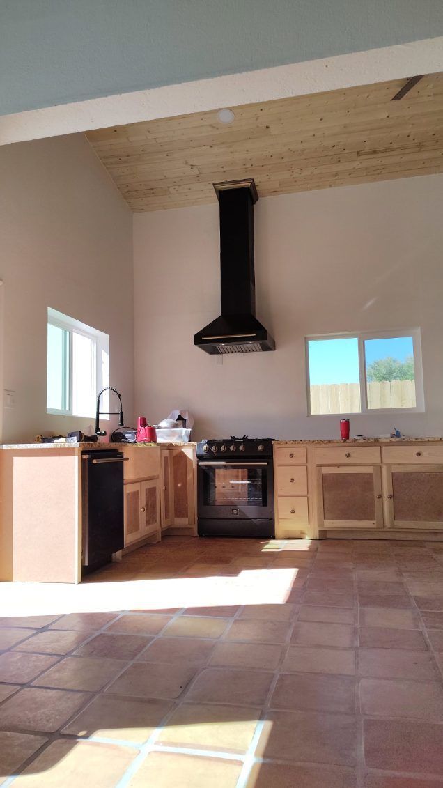 Kitchen interior with light-brown cabinets, black appliances, and terracotta tile floor.