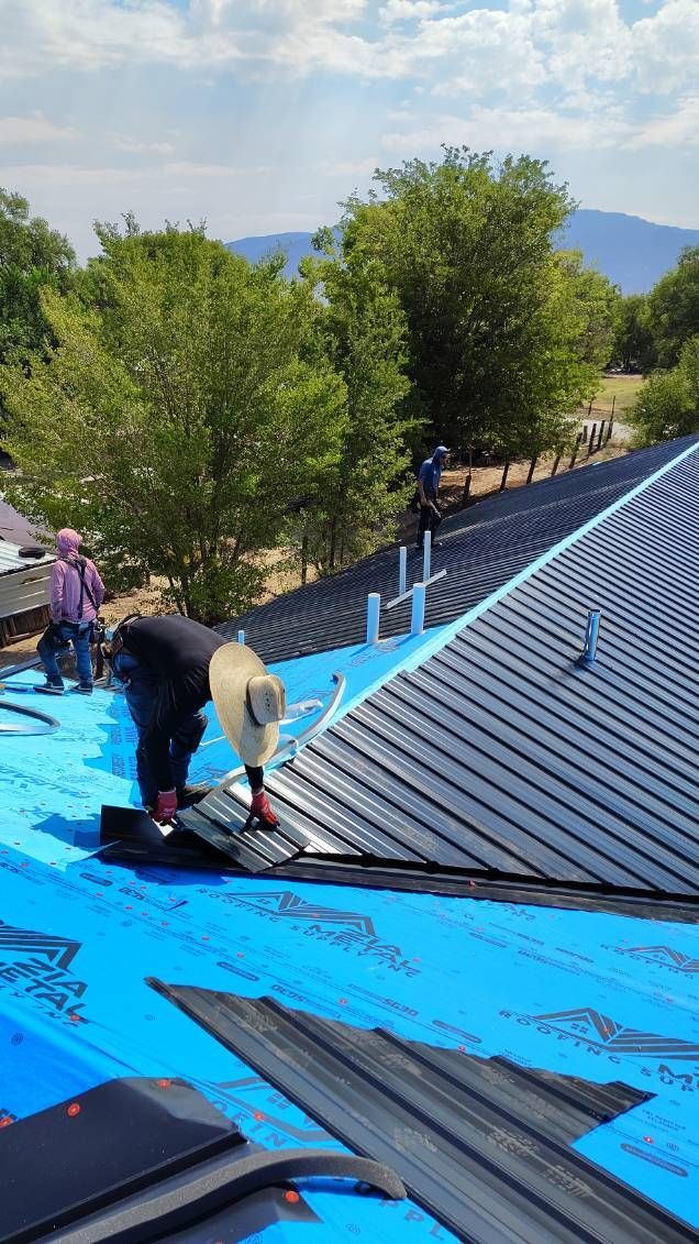 Roofers installing shingles on a blue underlayment on a sunny day.