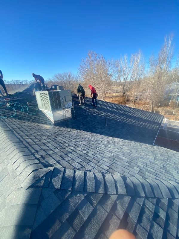 Workers on a rooftop, installing shingles. Sunny day, blue sky.