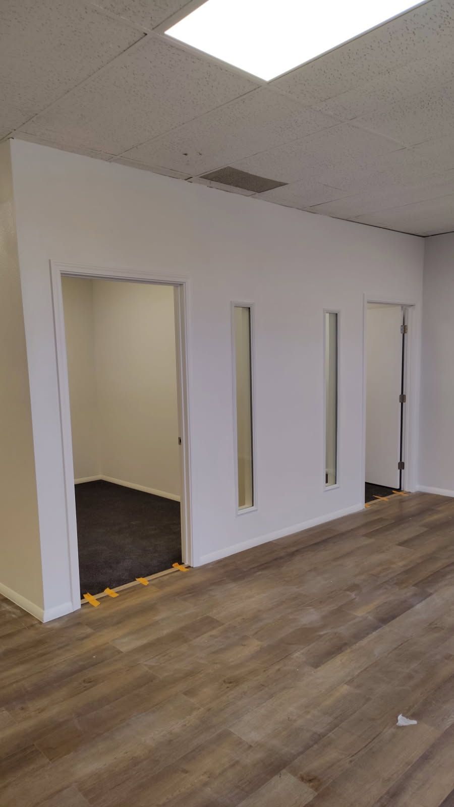 Interior with white walls, three doorways, and wood-look flooring. Two rooms are visible, one with dark flooring.