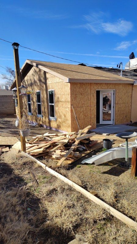 Construction of a small building, with exposed wood frame and sheathing, under a blue sky.