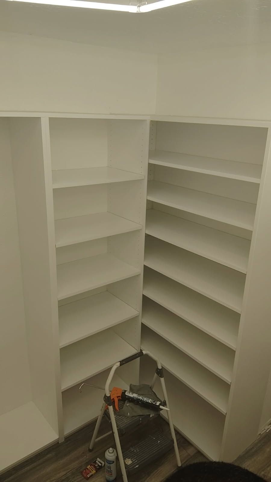 White shelving unit in corner of a room, with a step ladder.
