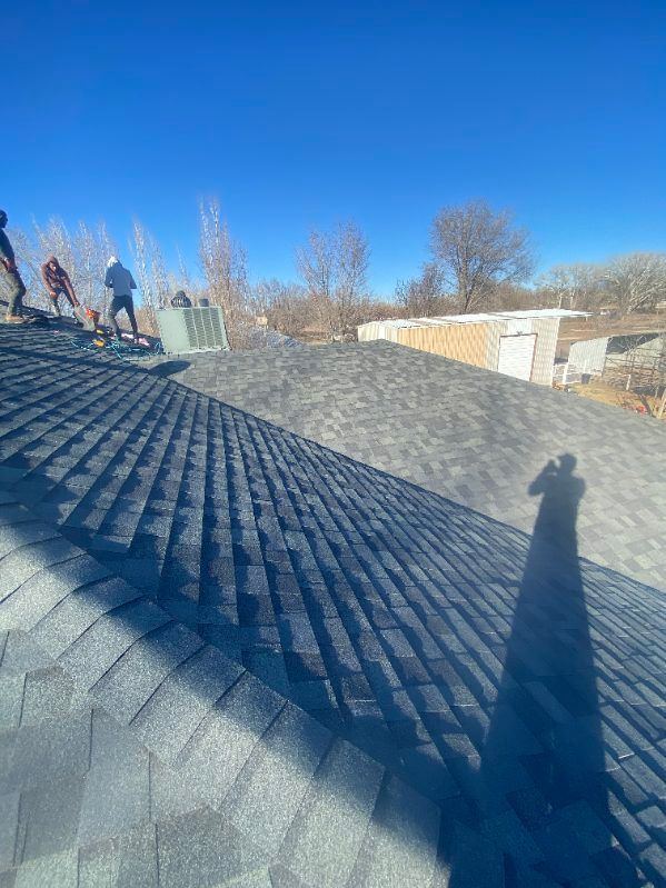 Roofers installing asphalt shingles on a sunny day.