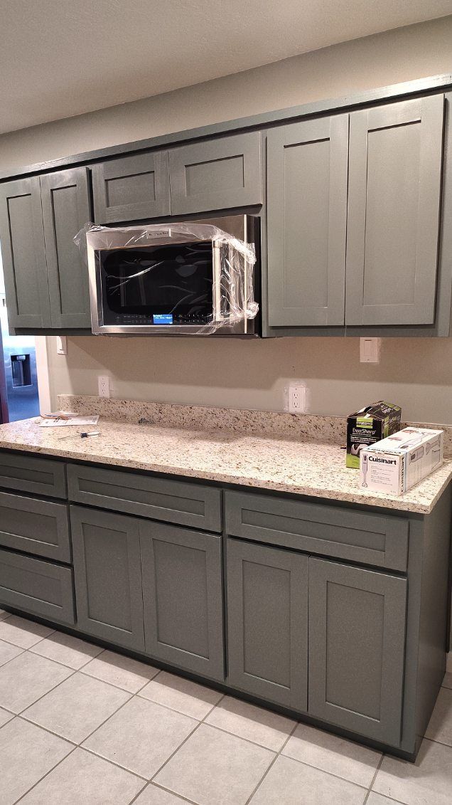 Gray kitchen cabinets with a microwave over a speckled countertop.