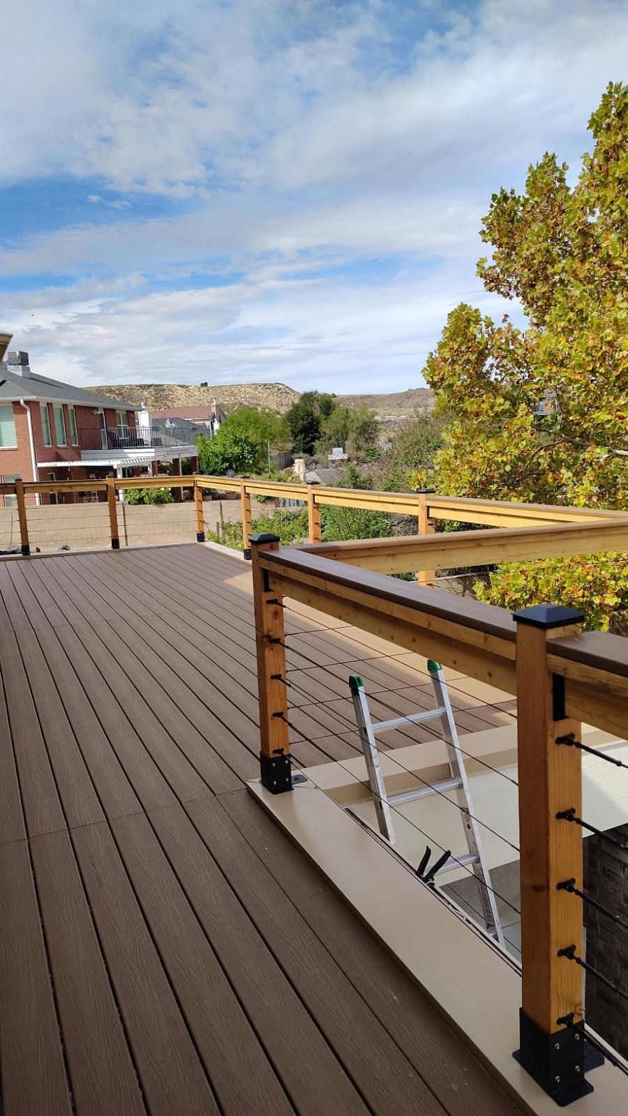 A wooden deck with a ladder, overlooking a view of buildings and trees under a cloudy sky.