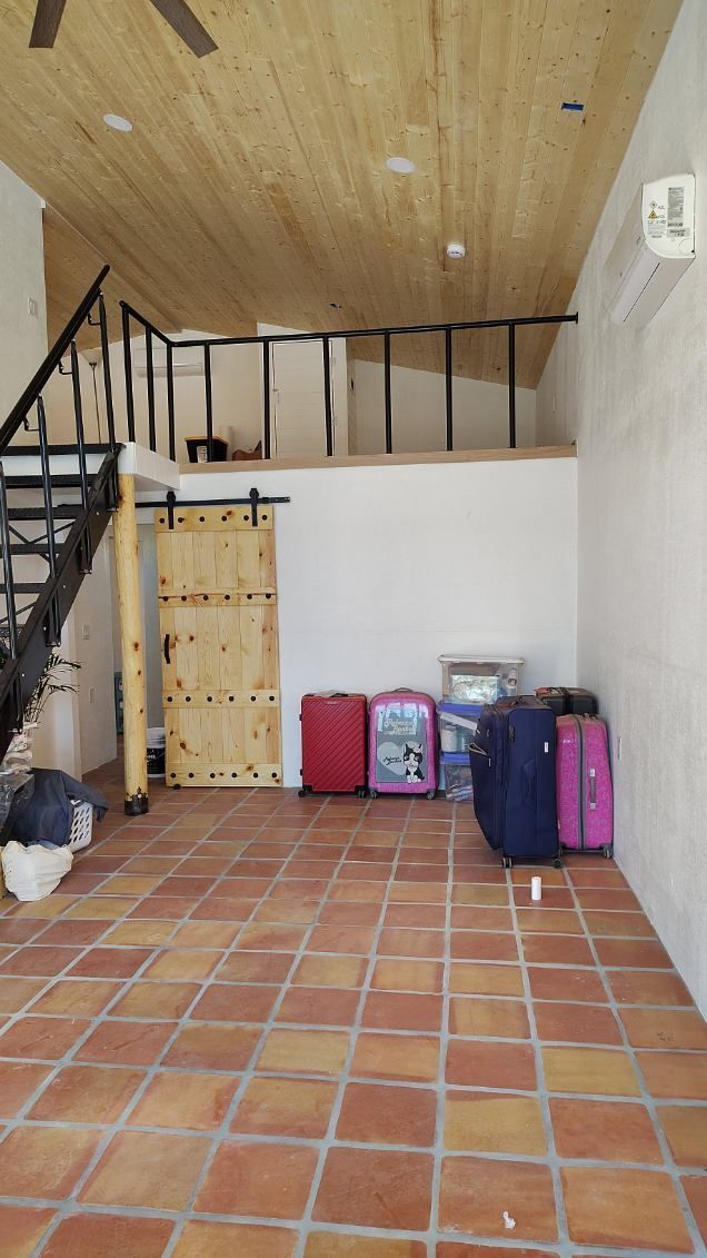 Interior with a loft, wood ceiling, tile floor, metal staircase, and luggage.
