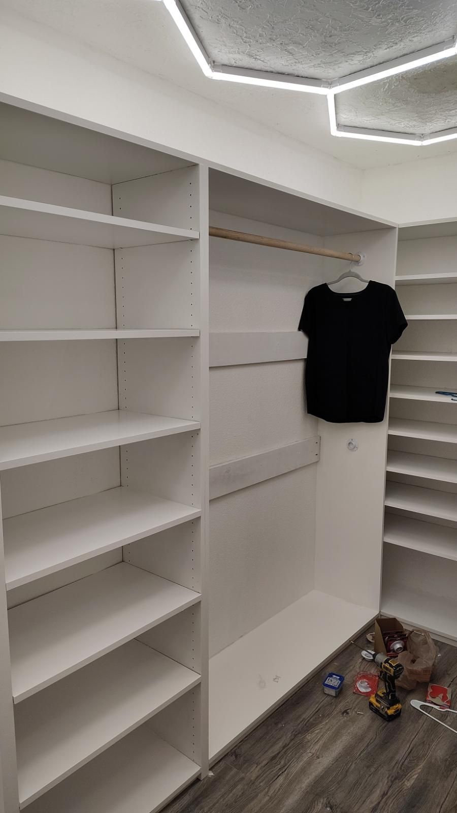 White closet with shelves and a hanging black shirt.