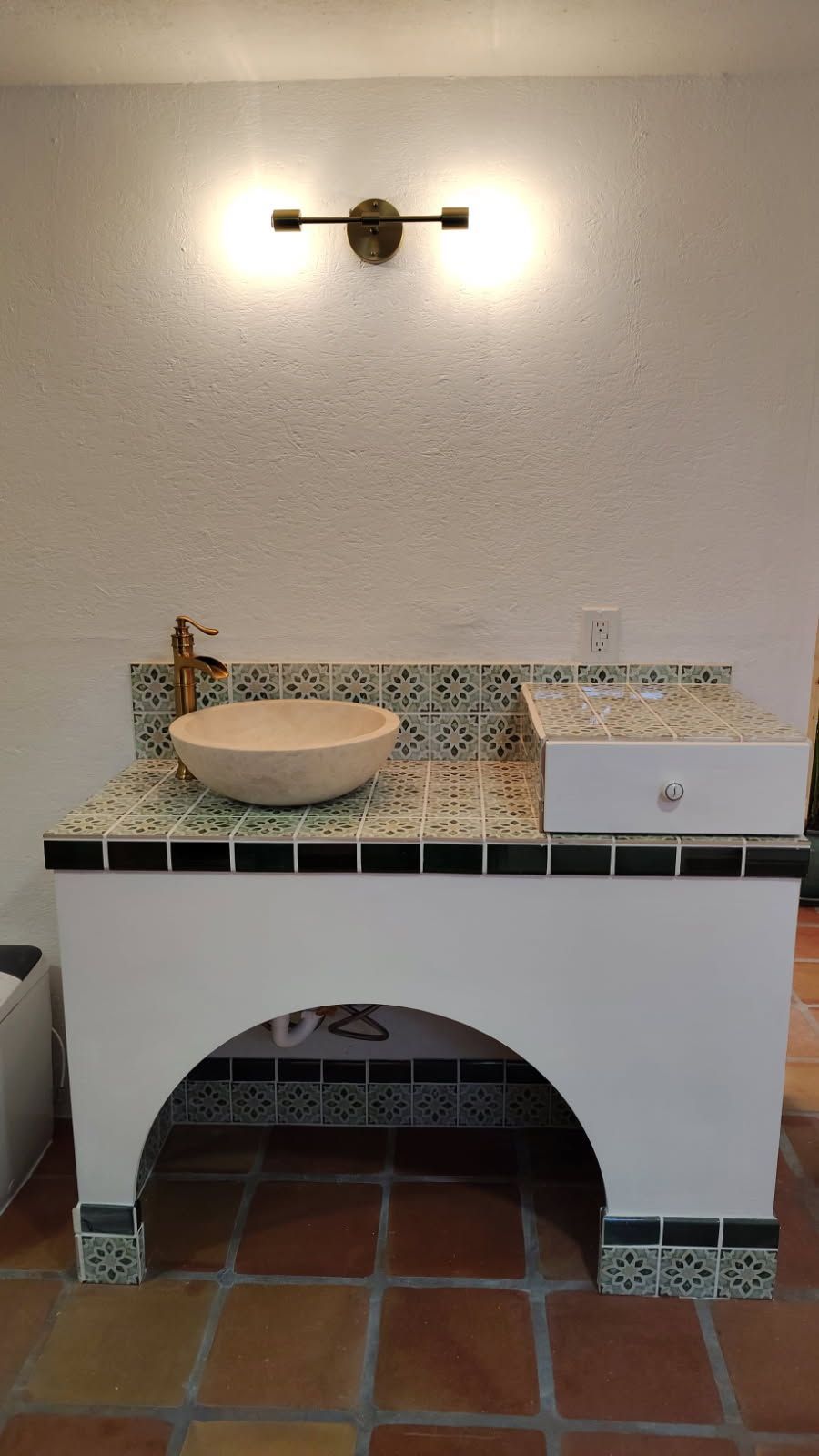 Bathroom sink with white cabinet, arched opening, and tiled countertop.