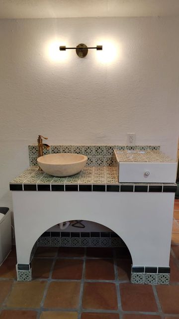 White and tiled bathroom vanity with arched opening, ceramic vessel sink, and gold faucet.
