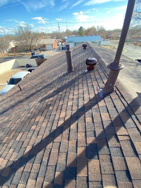 A rooftop with brown shingles and several vents under a blue sky.