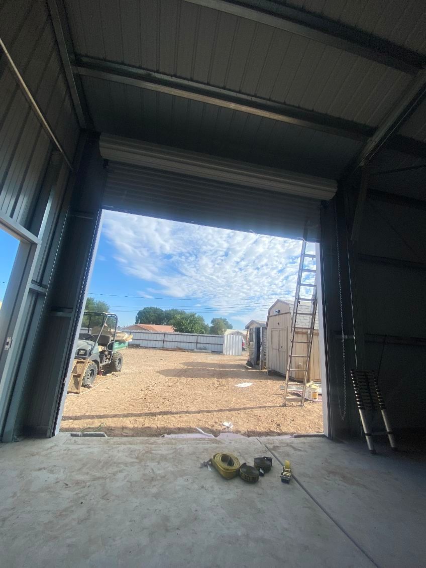 View from inside a metal building, looking out at gravel lot and sky through an open garage door.