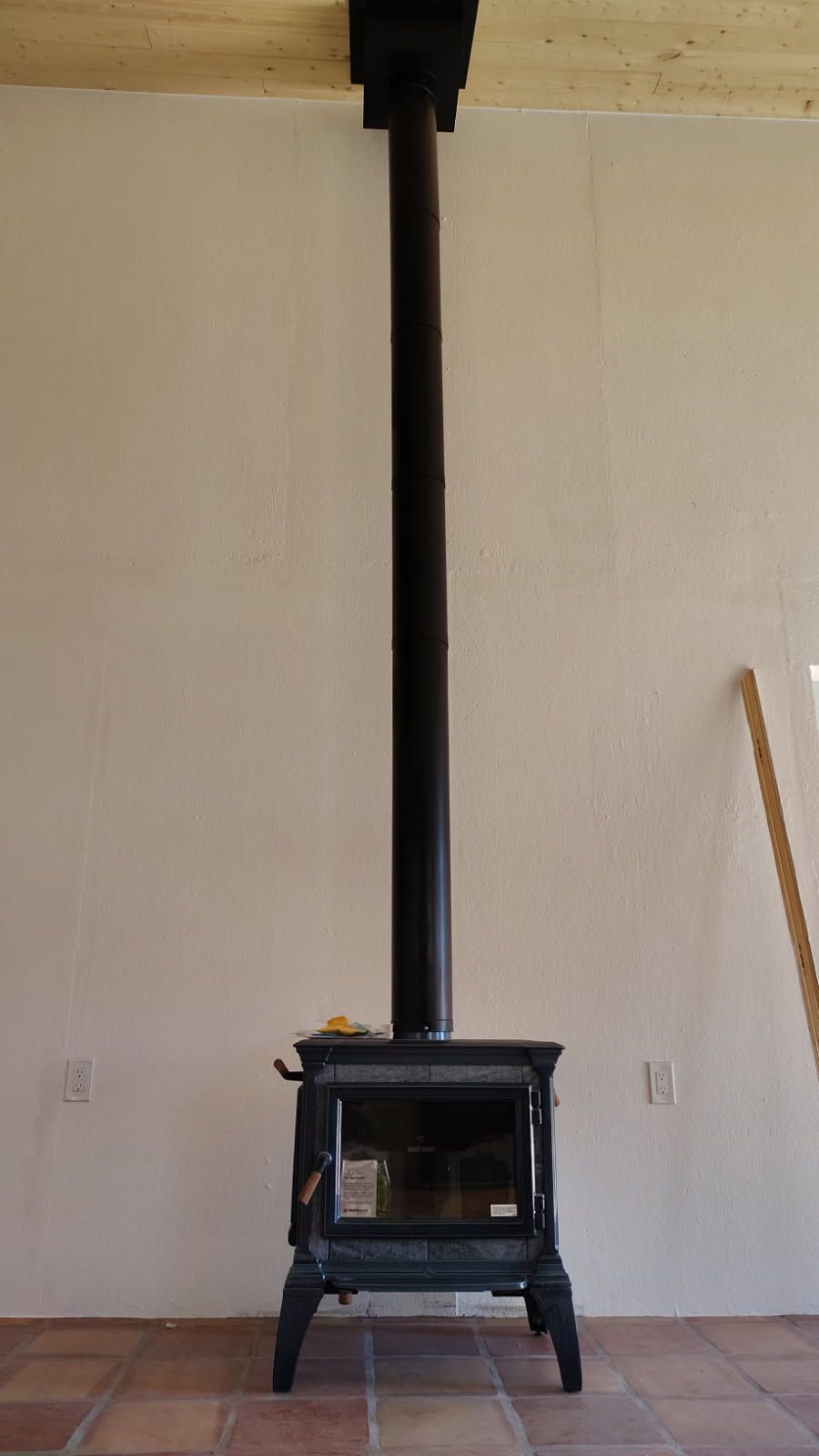 Black wood-burning stove with a tall pipe against a light-colored wall and terracotta tile floor.