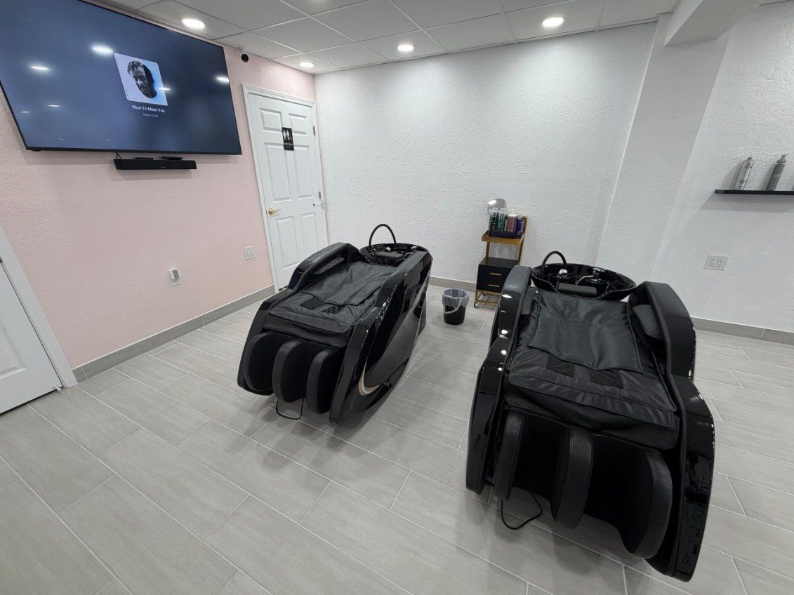 Two black massage chairs in a white-walled room with a television and door.