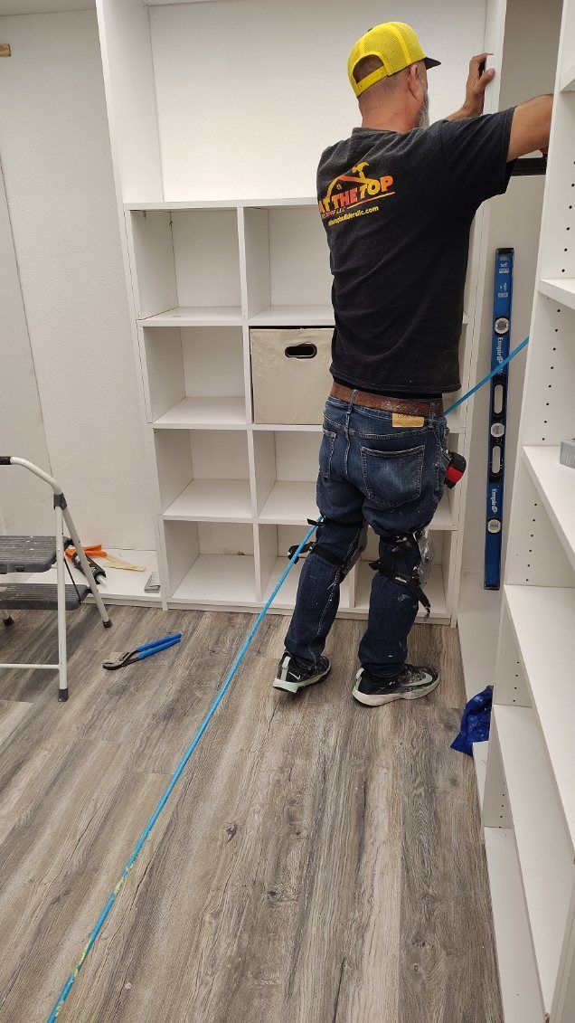 A person in a yellow hat installing a white closet shelving unit, using a level.