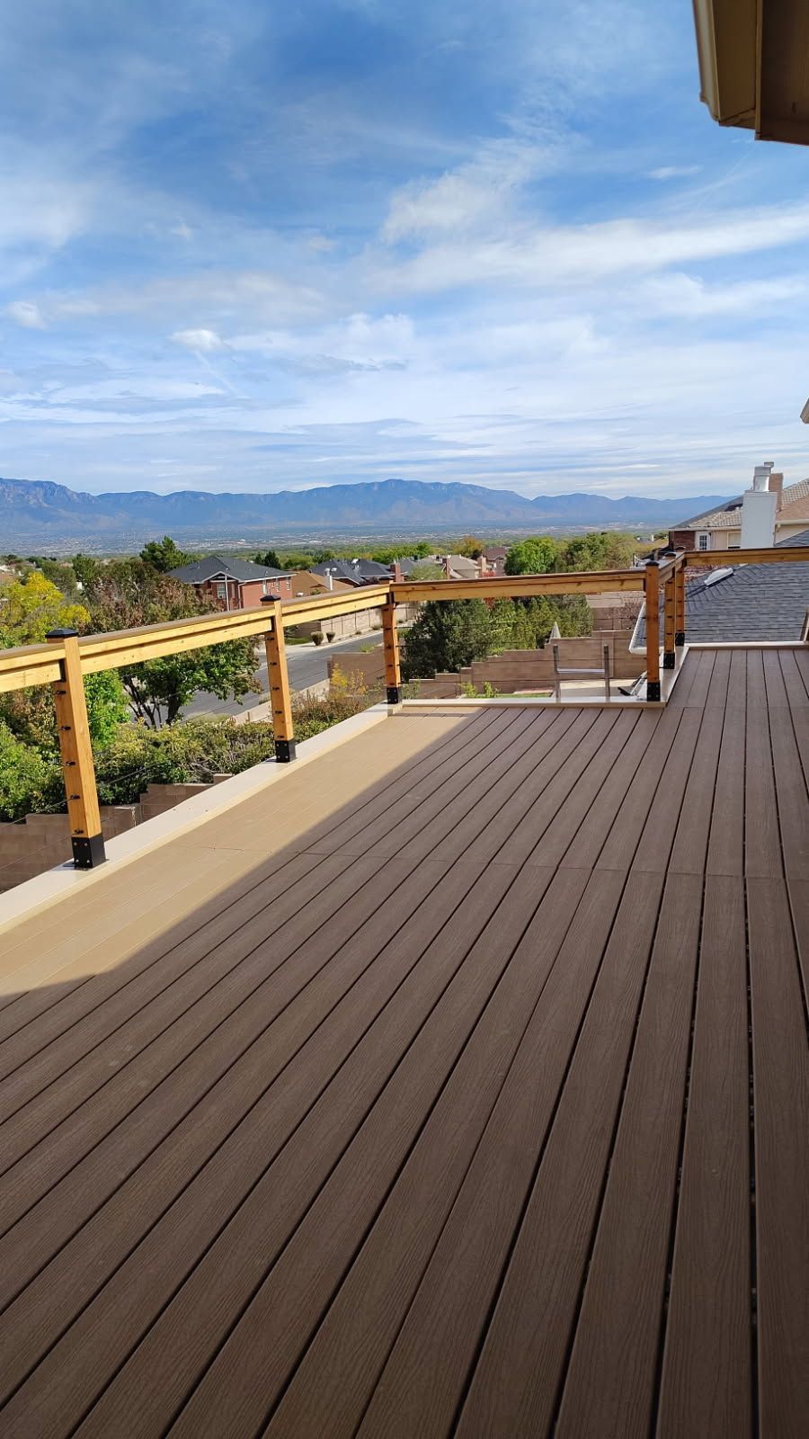 Wooden deck with pergola, overlooking a valley and mountains under a blue sky.
