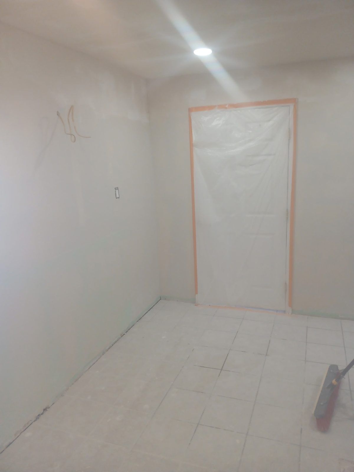 Empty room with white walls, unfinished door, and light on the ceiling. Flooring is covered with white tiles.
