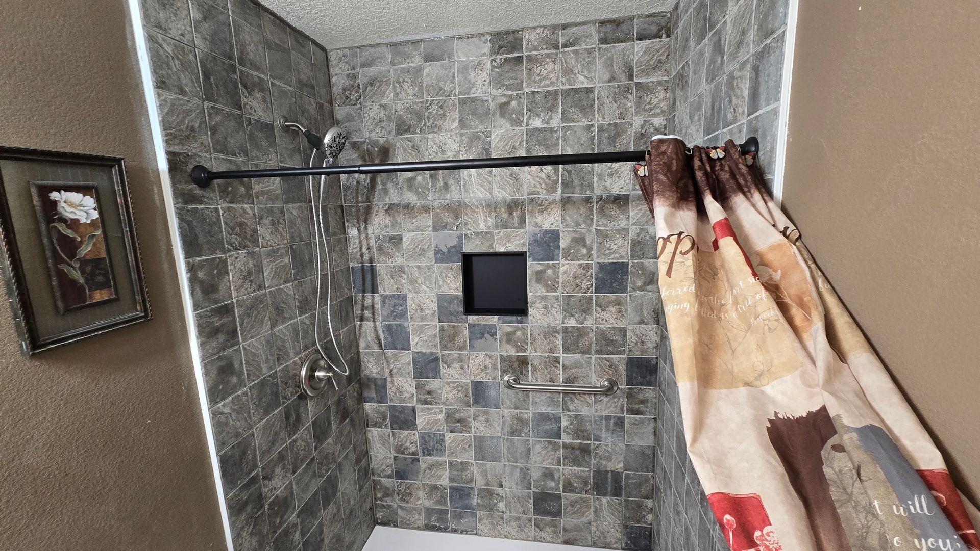 Shower with gray tile, brown shower curtain, and built-in shelf.