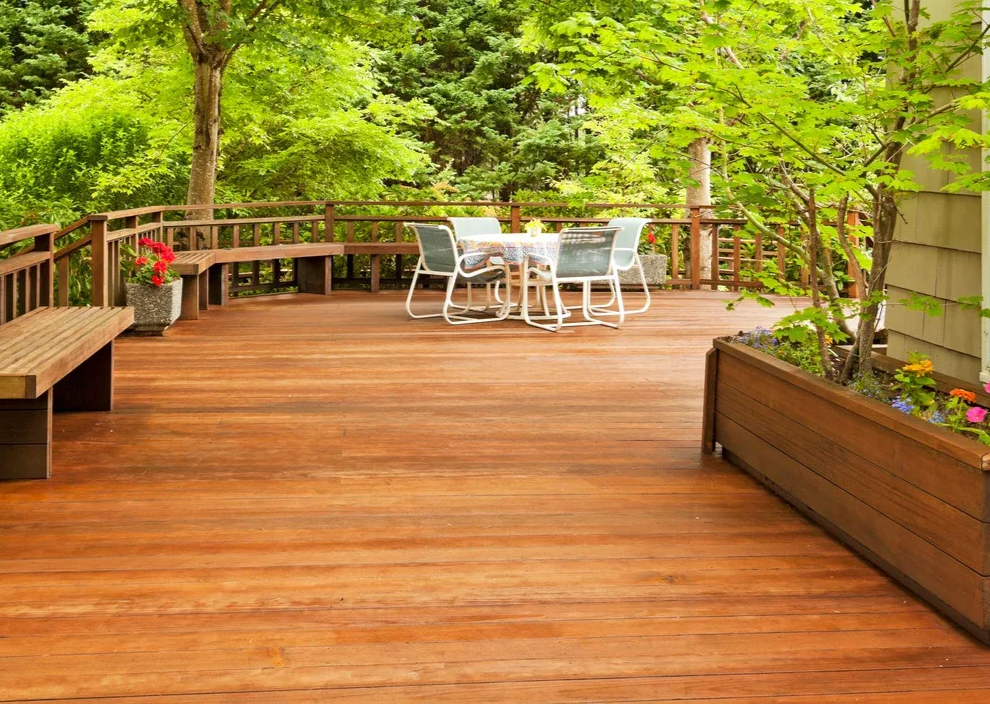 Wooden deck with benches, dining table, and potted plants, surrounded by lush green trees.