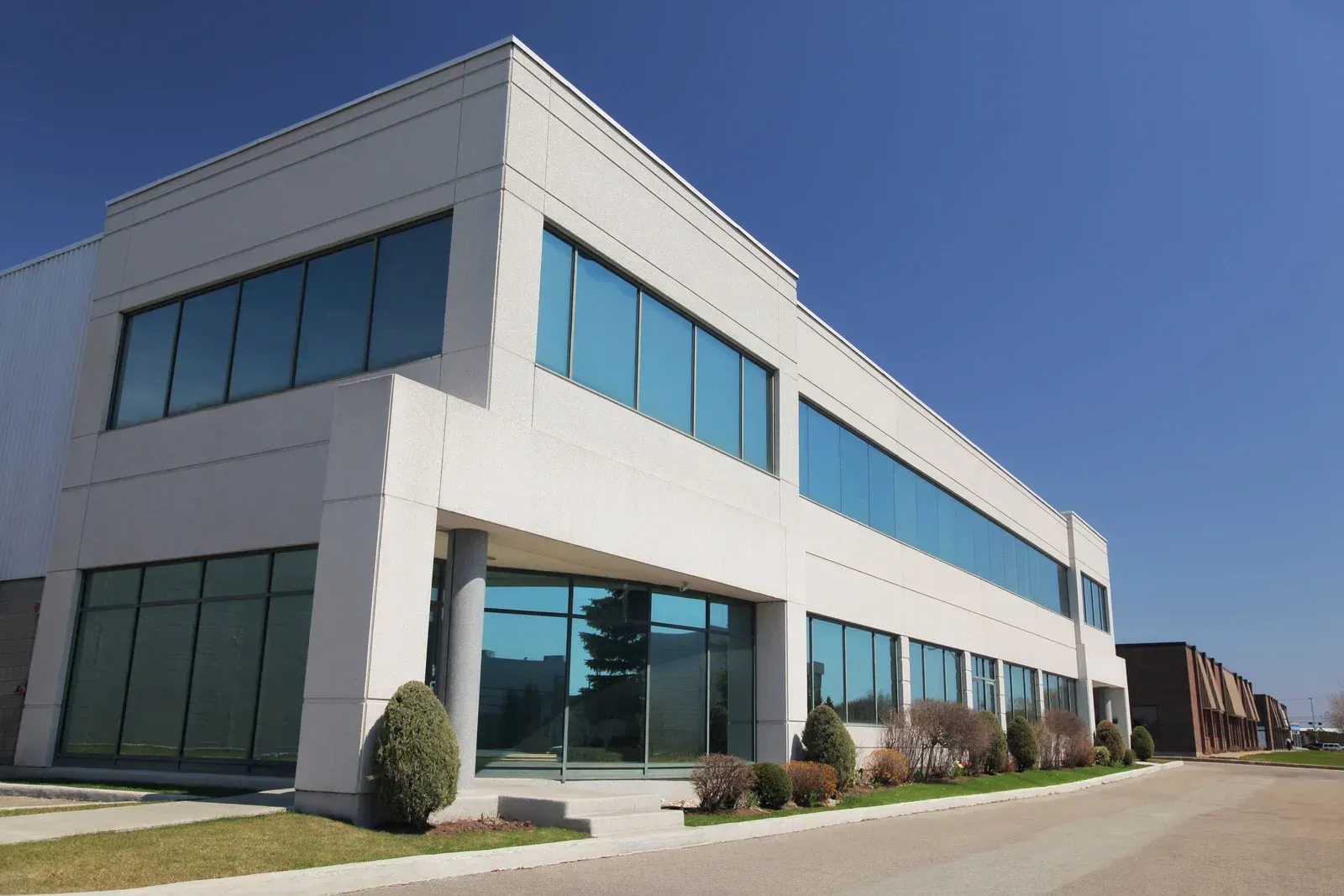 Modern two-story white building with blue-tinted windows, under a clear blue sky.