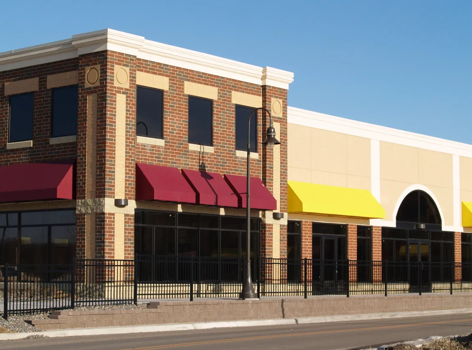 Brick and tan commercial buildings with red and yellow awnings, along a sidewalk.