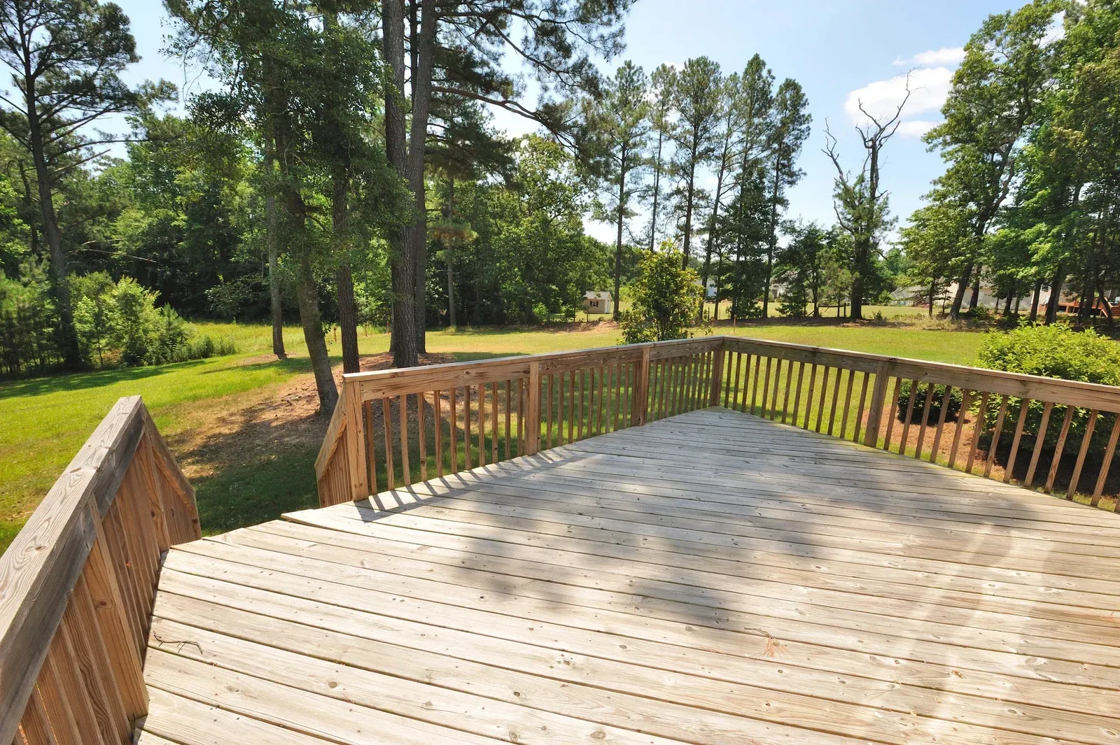 Wooden deck overlooking a grassy yard surrounded by trees on a sunny day.